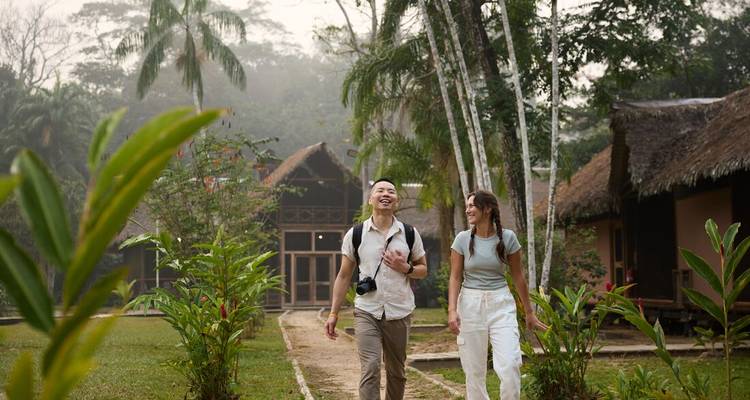 Una pareja pasea por un sendero del jardín rodeado de exuberantes plantas tropicales hacia cabañas de paja en la selva.