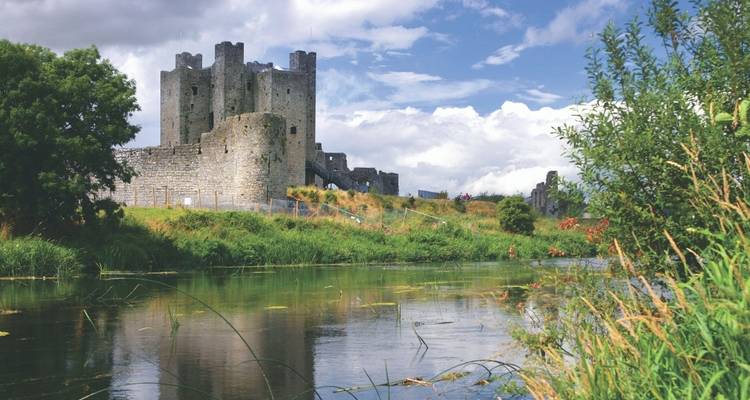 Historic castle ruins by a river under a blue sky.