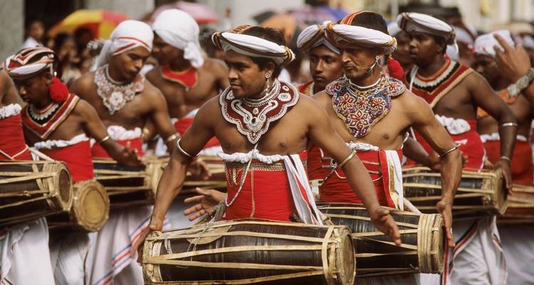 Obenfreie srilankische Trommler in aufwändigen Kostümen treten während einer lebendigen Parade auf.