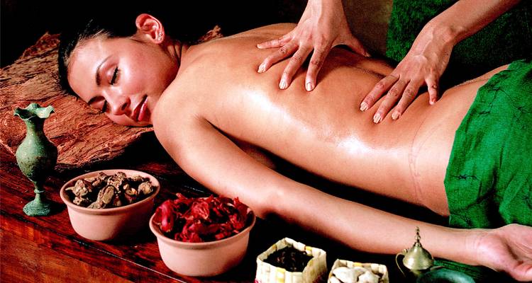 Eine Masseurin gibt eine Ölmassage umgeben von Kräutern in einer Spa-Umgebung.
