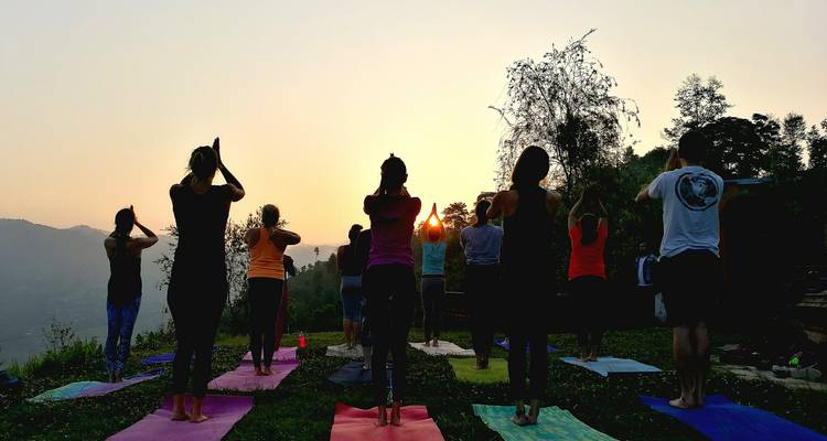 Practicantes de yoga recortados contra la luz sostienen poses de amanecer en colchonetas de colores vibrantes que dan a cerros brumosos.
