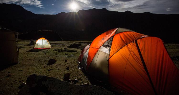 Tenten verlicht door maanlicht in een bergachtig gebied.