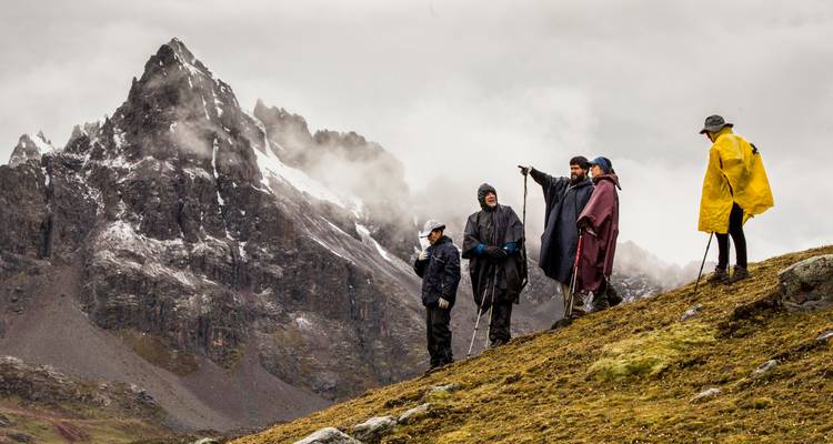 Groep wandelaars in poncho's met een dramatische bergachtergrond.