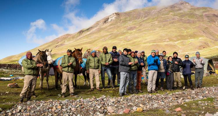 Een grote groep mensen en paarden in een bergomgeving.