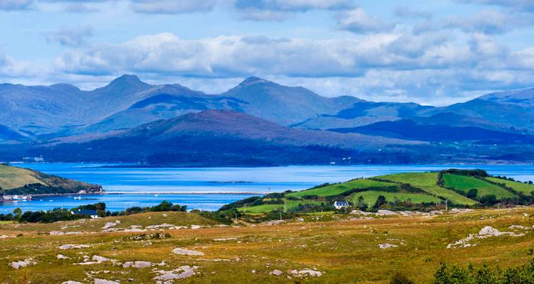 Vue panoramique du paysage de Connemara avec baie bleue, champs verts ondulants et chaîne de montagnes lointaine