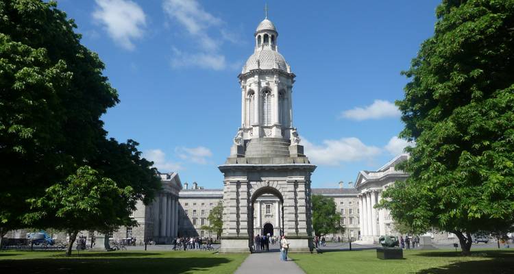 Stone Campanile of Trinity College Dublin framed by manicured lawns and visiting tourists