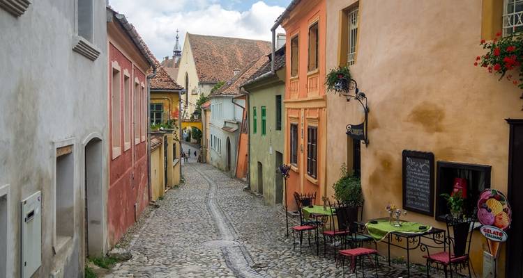 Kopfsteinpflasterstraße gesäumt von bunten Häusern und Außentischen.