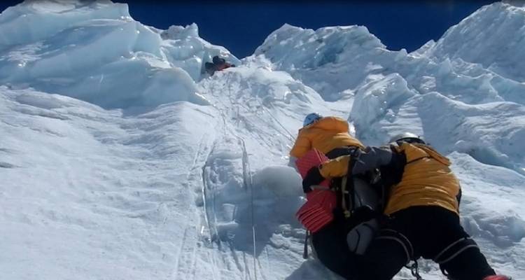 Klimmers met uitrusting die een besneeuwde helling beklimmen.