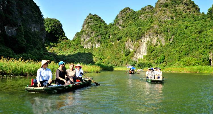 Touristen rudern mit Booten durch einen ruhigen Fluss, der von Kalkstein-Karst flankiert wird.