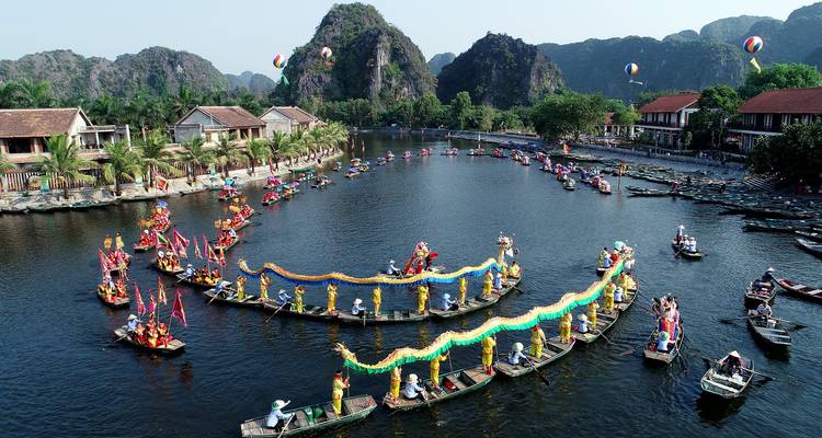 Festzug mit Booten und bunten Drachen in malerischer Flusslandschaft.
