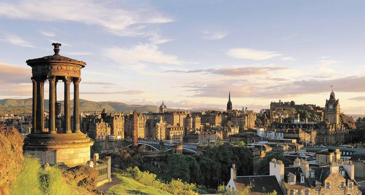 Skyline de la ville dorée avec monuments et ponts vue d'une colline verdoyante au coucher du soleil.