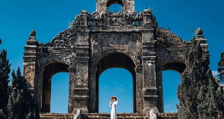 Eine Person, die vor einer alten Steinstruktur mit Bögen steht.