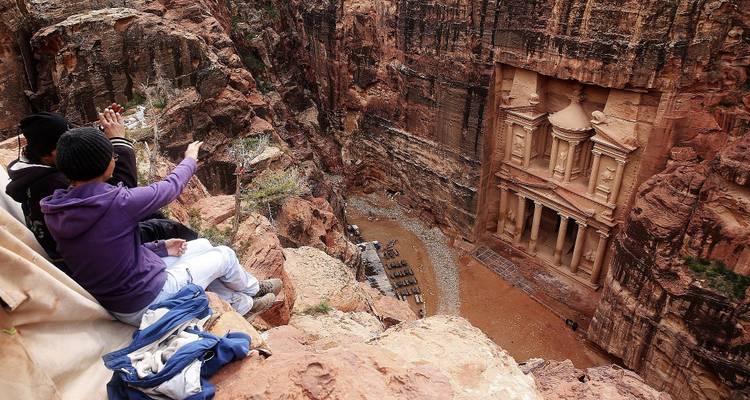 People sitting on a cliff overlooking the Petra ruins.
