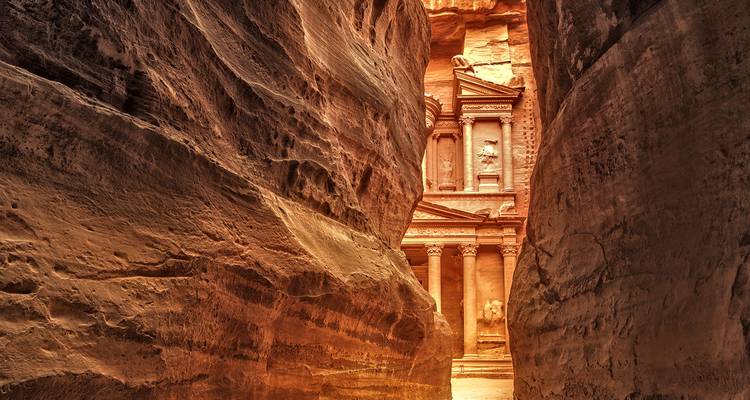 The Petra Treasury viewed through a narrow rock canyon.