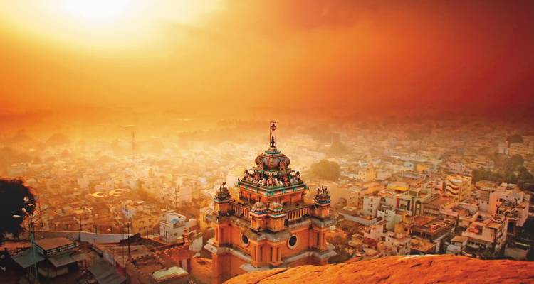 Vue panoramique d'un temple au coucher du soleil avec un ciel orange et un paysage urbain.
