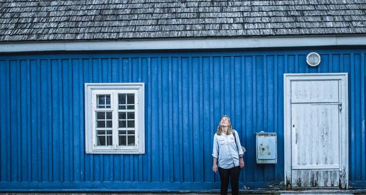 Persoon die buiten voor een blauw houten huis staat en omhoog kijkt.