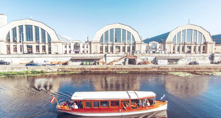 Zicht op een modern marktgebouw langs een rivier met een voorbijvarende boot.