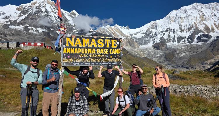 Group of trekkers celebrating at Annapurna Base Camp sign with snow-clad peaks towering behind