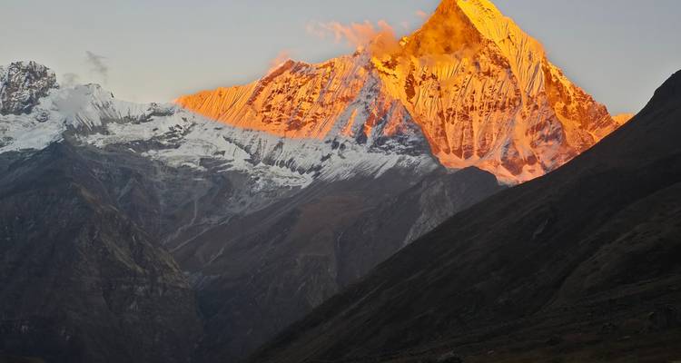 Golden alpenglow illuminating Machapuchare peak at sunrise above dark valleys