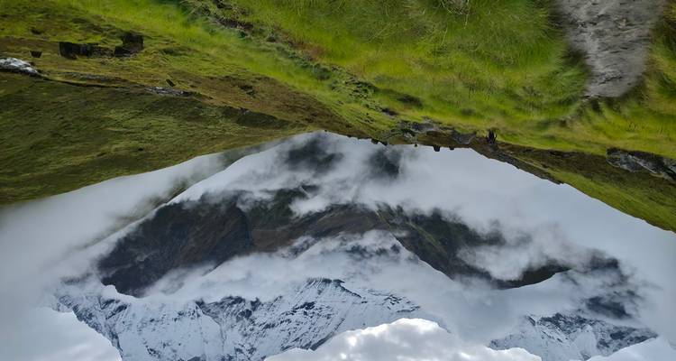 Misty mountain valley with lush green slopes and clouds swirling beneath snowy summits