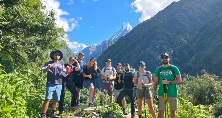 Hiking group posing on lush trail with fishtail mountain towering in the background