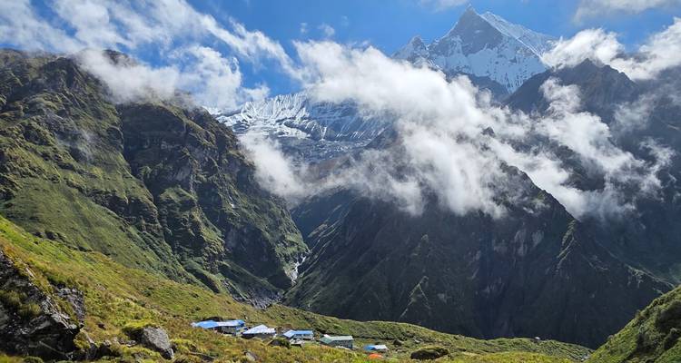 Clouds drifting across steep green slopes below a sharp snow-clad Himalayan peak