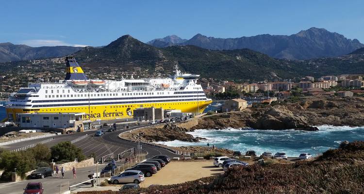 Un grand ferry amarré dans une ville côtière avec un arrière-plan montagneux.