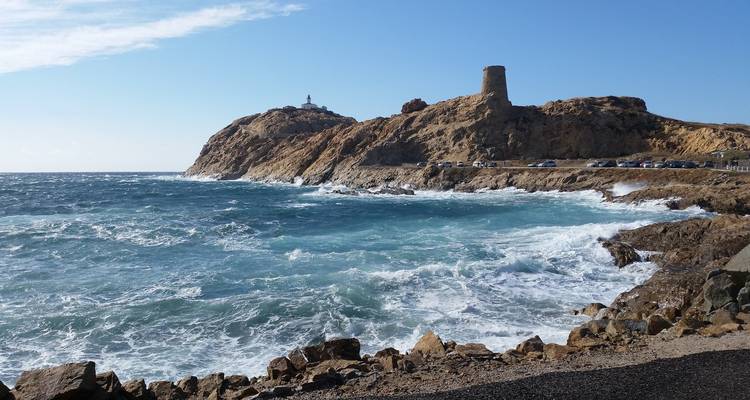 Des vagues qui se brisent contre des falaises rocheuses avec une structure historique au sommet.
