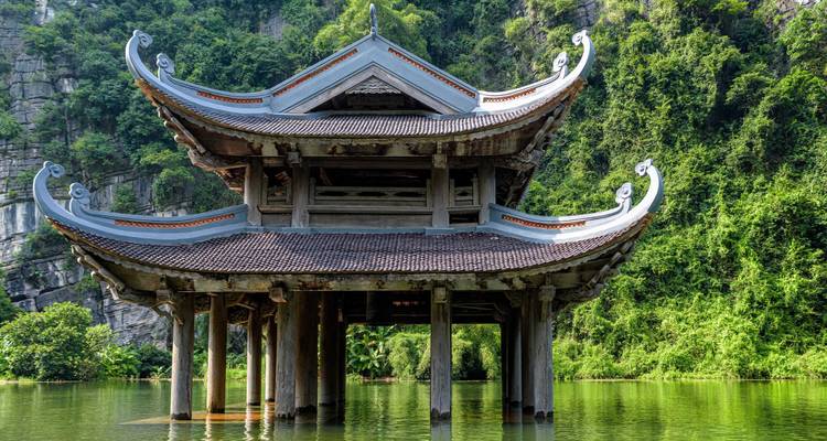 Traditioneller Pavillon im Pagodenstil erhebt sich aus ruhigem grünem Wasser vor Kalksteinklippen und üppigem Wald.