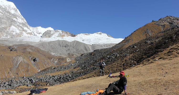 Dos personas descansando en una ladera con montañas nevadas al fondo.