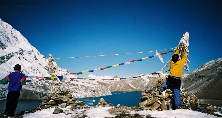 Deux personnes avec des drapeaux de prière près d'un lac de montagne.