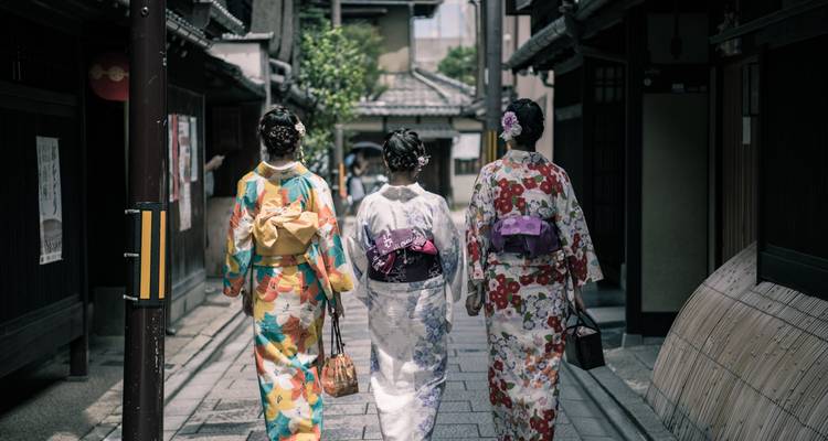 Trois femmes en kimonos colorés marchant dans une rue japonaise traditionnelle.