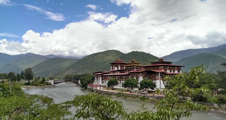 Punakha Dzong en la orilla de un río rodeado de montañas exuberantes y un cielo nublado.
