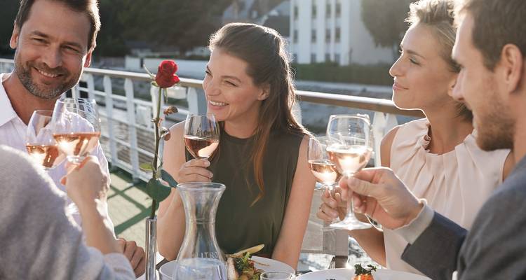 Grupo de amigos brindando with vino rosado en la cubierta de un crucero fluvial durante el almuerzo