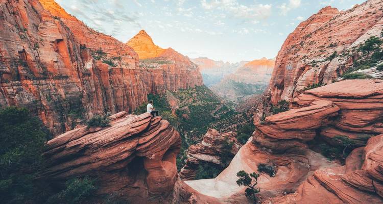 Une vue panoramique du parc national de Zion avec une personne debout sur une formation rocheuse surplombant un canyon.