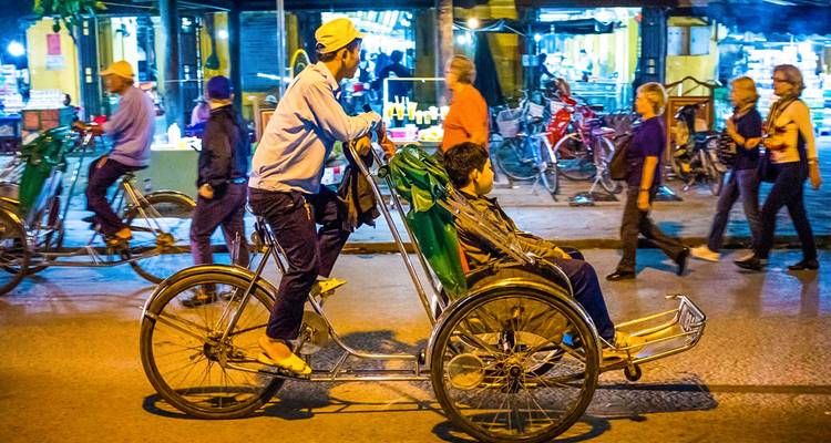 Riksja bestuurder die een rit geeft in een drukke straat 's nachts.