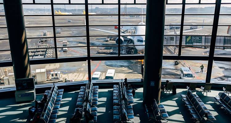 Large airport gate lounge with rows of empty seats overlooking an aircraft through floor-to-ceiling windows.