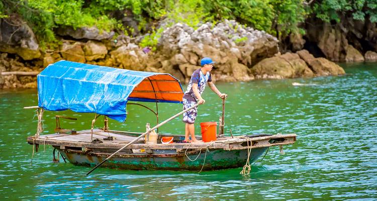 Persoon die een boot roeit in turquoise water omringd door kalksteenrotsen.