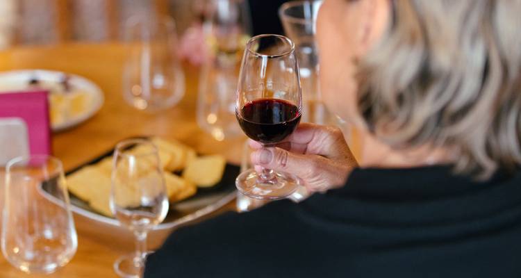 Gros plan d'une personne tenant un verre de vin rouge lors d'une séance de dégustation à une table en bois.