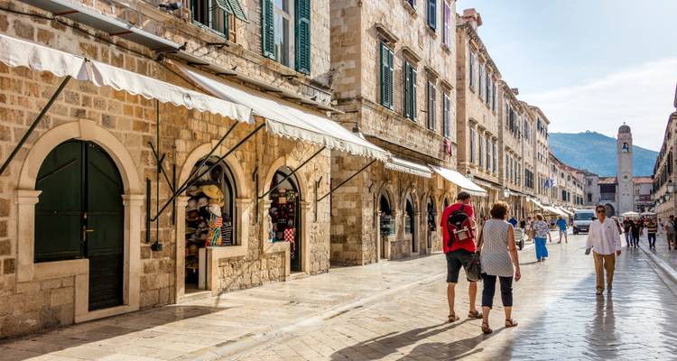 Les piétons se promènent le long de la Stradun en calcaire de Dubrovnik, bordée de bâtiments historiques en pierre et de devantures commerciales.