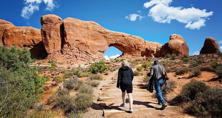 Twee mensen die naar een grote rotsboog toe lopen.