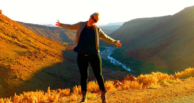 Frau posiert fröhlich in einer Wüstenschlucht mit weiten Ausblicken.