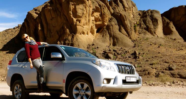 Person, die sich an einen SUV in einer Wüstenlandschaft mit Felsformationen lehnt.