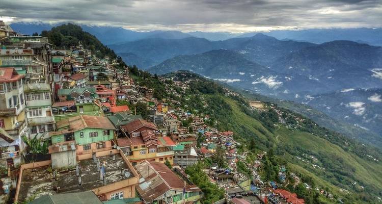 Blick auf eine hügelige Stadt mit Wolken und fernen Bergen.