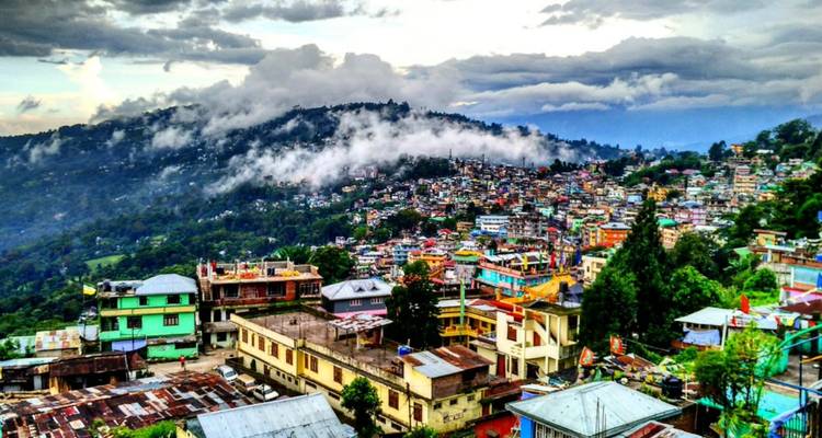 Hügelige Stadt mit bunten Häusern und Bergkulisse.