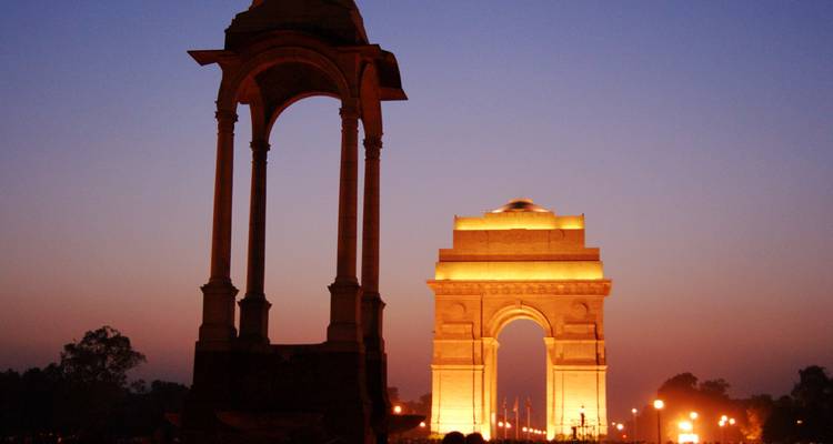 Beleuchtetes India Gate mit Menschen bei Sonnenuntergang.