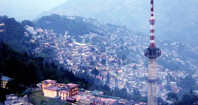 Eine Stadtansicht mit einem hohen Turm inmitten grüner Hügel und Häuser.