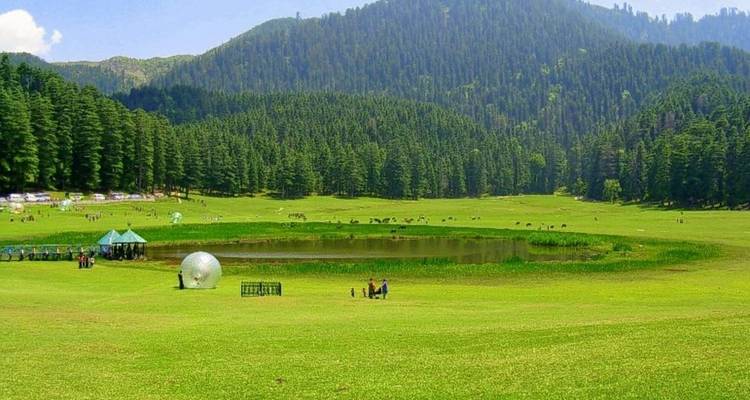 Weitläufiges grünes Tal mit kleinem See, umgeben von Bäumen und Menschen in der Ferne.