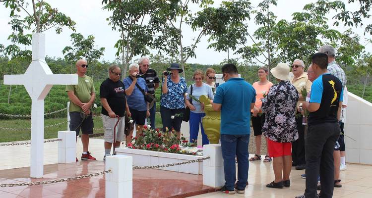 Visitors gathered around a memorial cross and flower bed at a historic battlefield site in Vietnam.