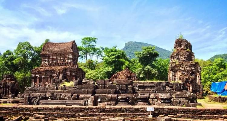 Ruins of ancient brick Hindu temples of My Son Sanctuary surrounded by lush green forest and blue skies.